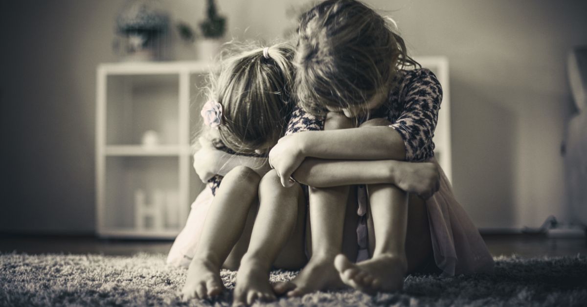 Two young girls sitting with their heads on their knees, crying and looking sad.