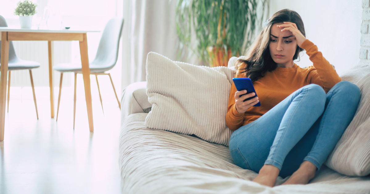 Woman on a couch looking worried while checking her phone — preparing digital accounts and online legacy.