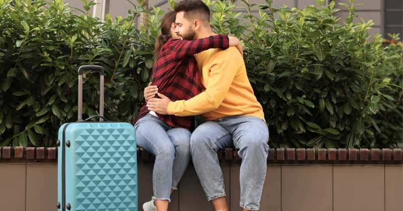 Couple embracing beside luggage while navigating grief and international funeral arrangements across borders.