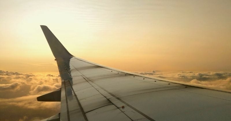 View from an airplane window overlooking the wing during a flight at sunset.